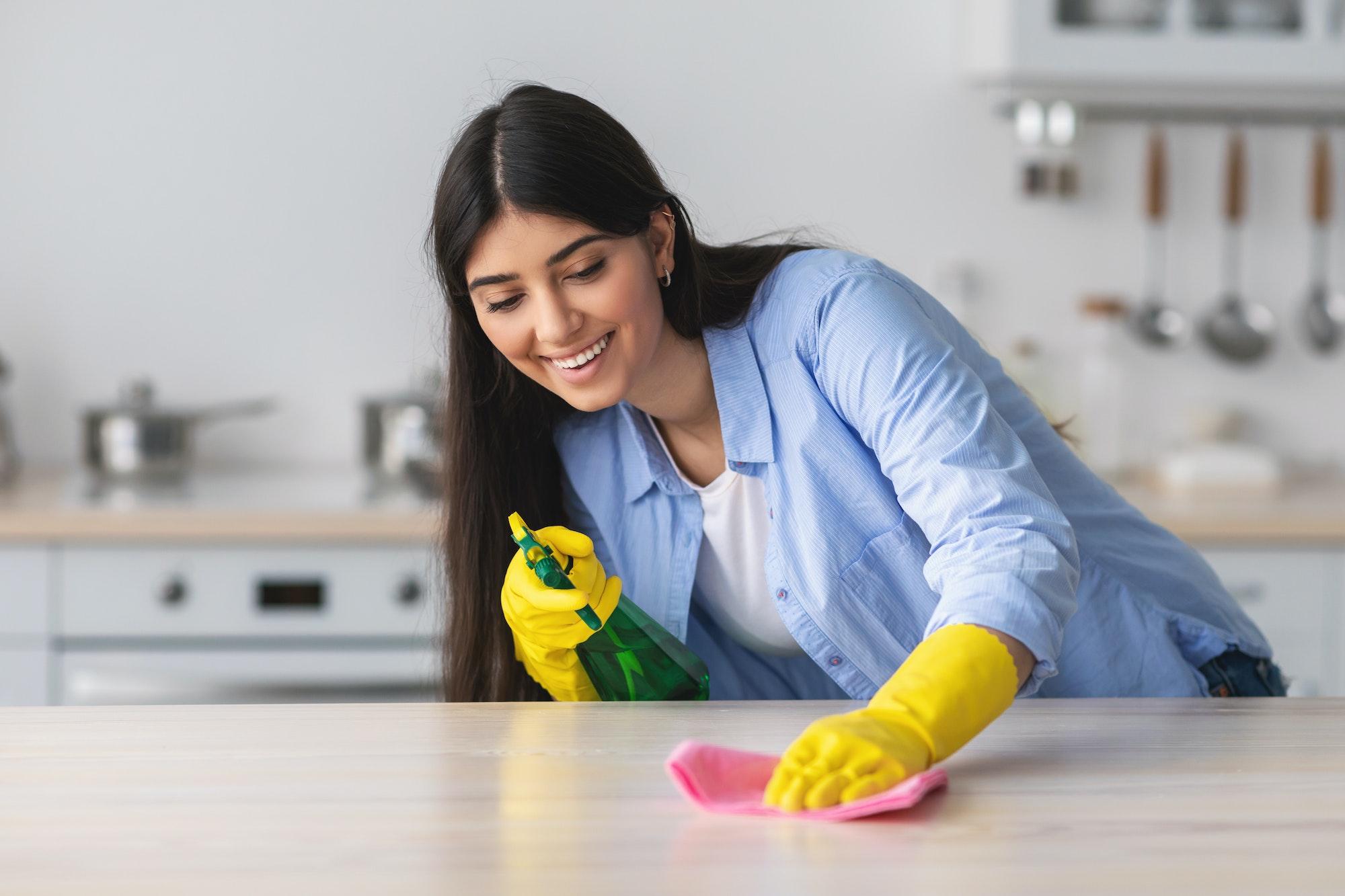 Cheerful young woman cleaning table with cloth