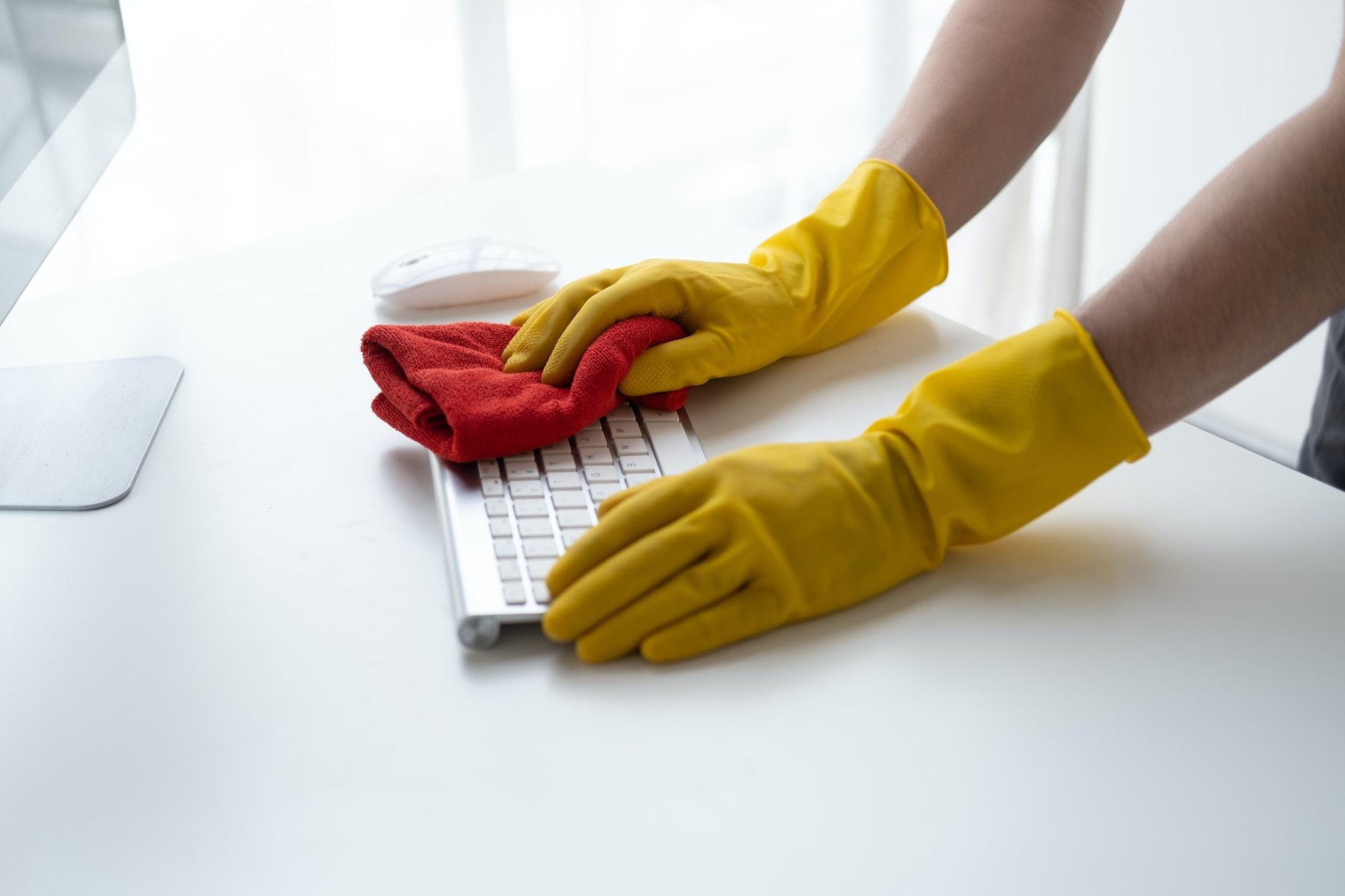 Close up view of man cleaning keyboard computer using clothes. Cleaning office desk concept.
