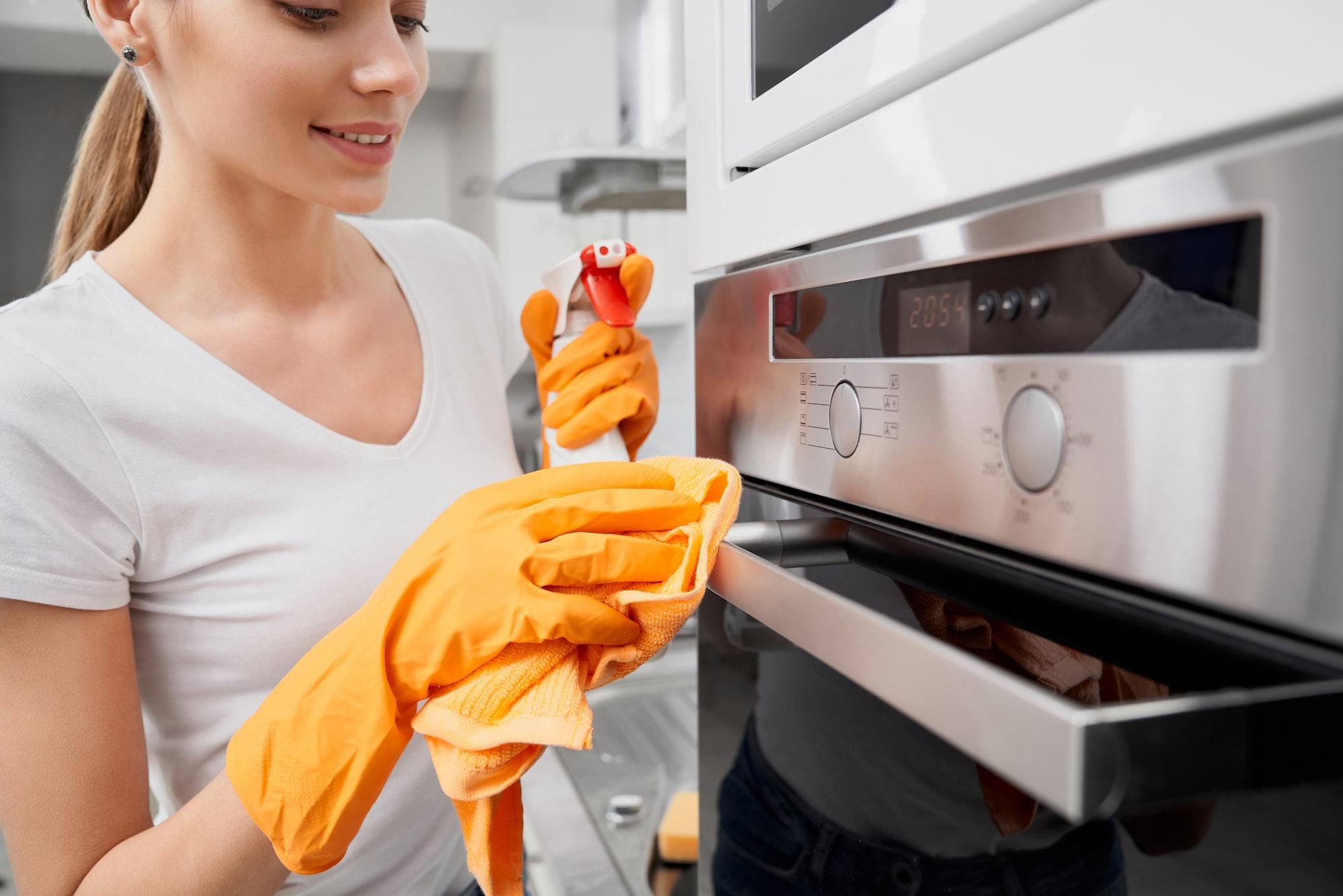 Smiling young woman cleaning oven with detergent